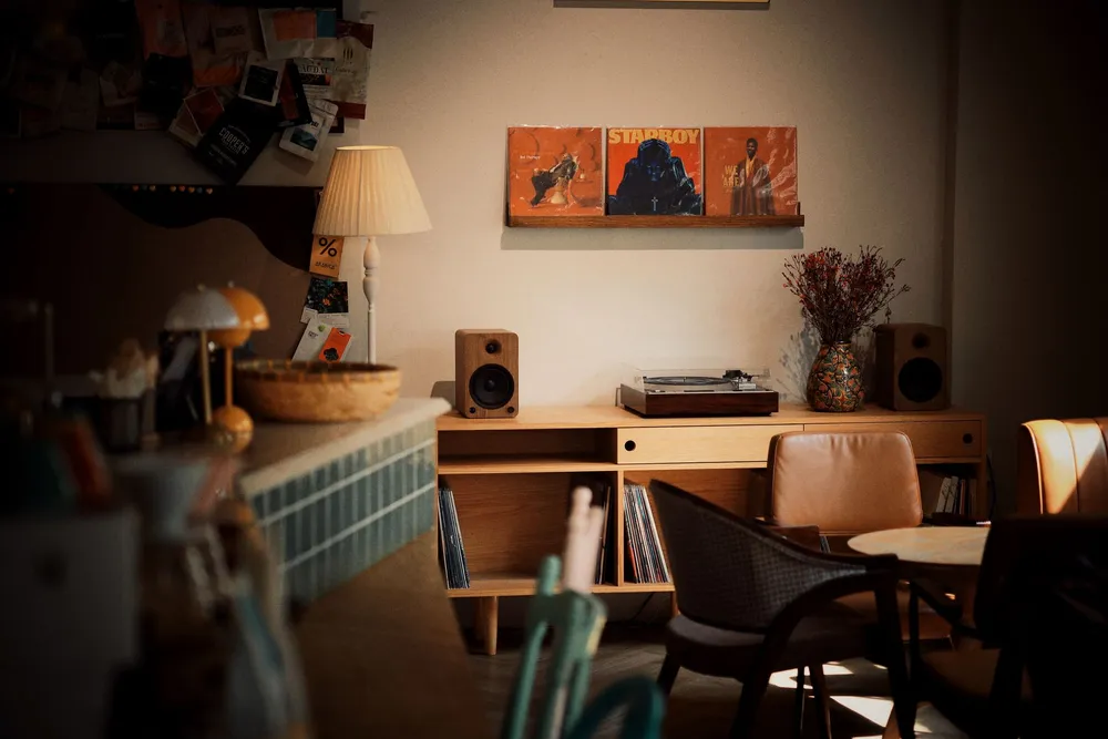 Deux enceintes bibliothèque en bois posées sur un meuble bas à côté d'une platine vinyle, dans un petit salon aux affiches encadrées